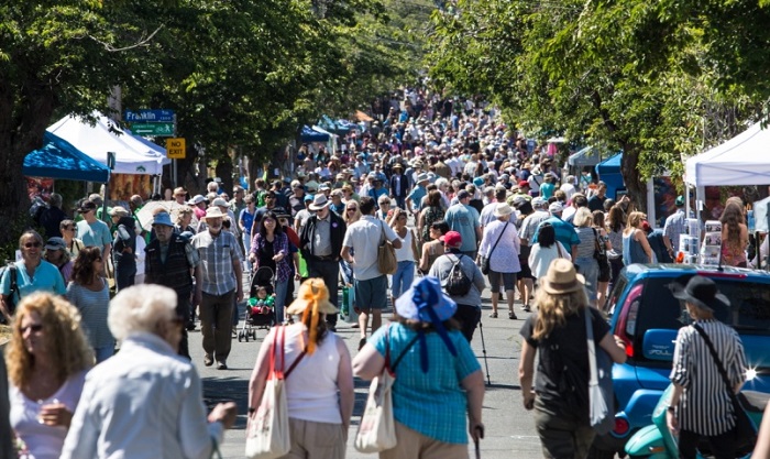 City street surrounded by greenery and crowded with people who are shopping at the artisan stands lining the road.